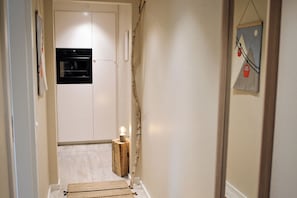 Ein schmaler Flur mit Holzboden, einem kleinen Tisch mit Lampe und einer Tür zu einem schwarzen Gerät.