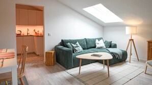 Un salon moderne avec un canapé vert, une petite table ronde, une lampe et une lucarne.