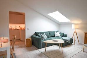Ein modernes Wohnzimmer mit einem grünen Sofa, einem kleinen runden Tisch, einer Lampe und einem Dachfenster.