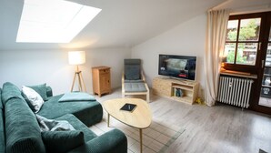 Un salon comprenant un canapé, un fauteuil, une table, une lampe, un téléviseur et une fenêtre avec des rideaux.