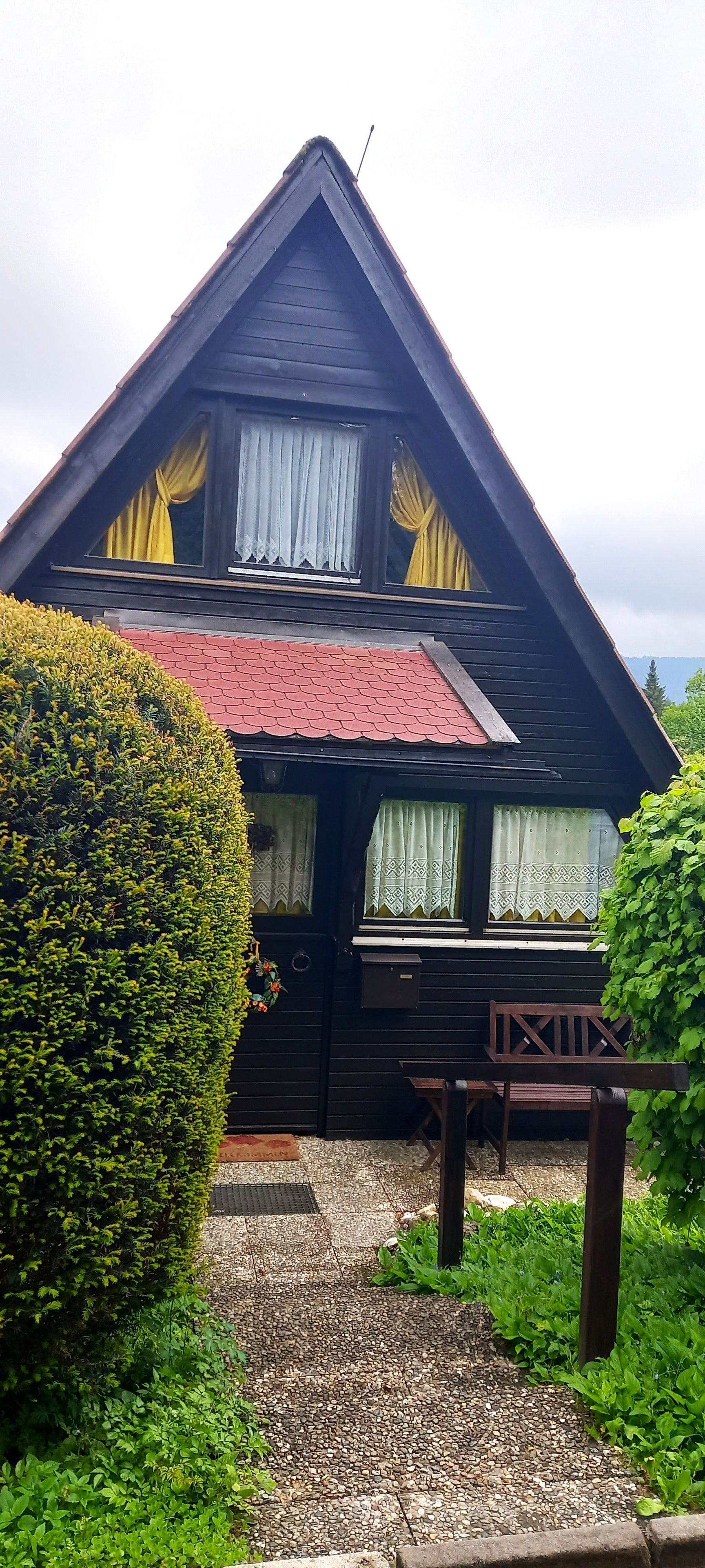 A two-story wooden house with a red roof, a balcony, and a well-maintained garden.