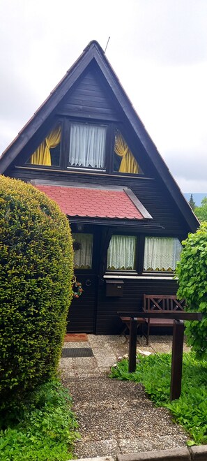 Una casa de madera de dos pisos con techo rojo, un balcón y un jardín bien cuidado.