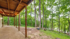 Un espacio al aire libre techado con piso de concreto, vigas de madera y vista a un área boscosa.