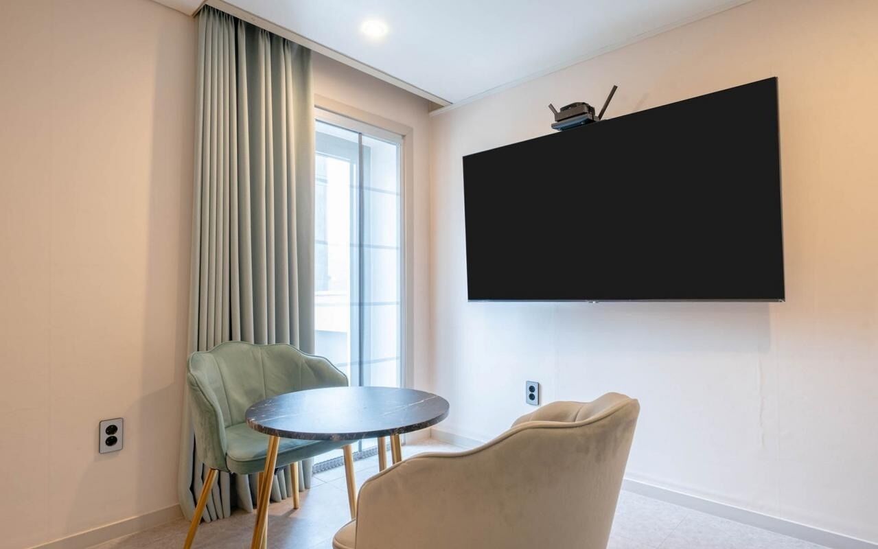 Una habitación con un ventanal grande, un televisor de pantalla plana en la pared, una mesa redonda y dos sillas.