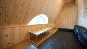 Una habitación con paredes de madera, un banco, un sofá negro y un tragaluz.