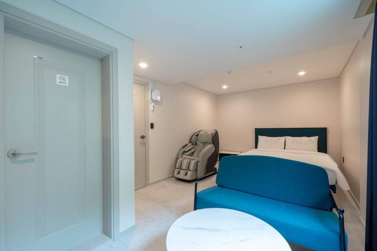 A hotel room with a bed, a massage chair, a small round table, and a door with a sign.