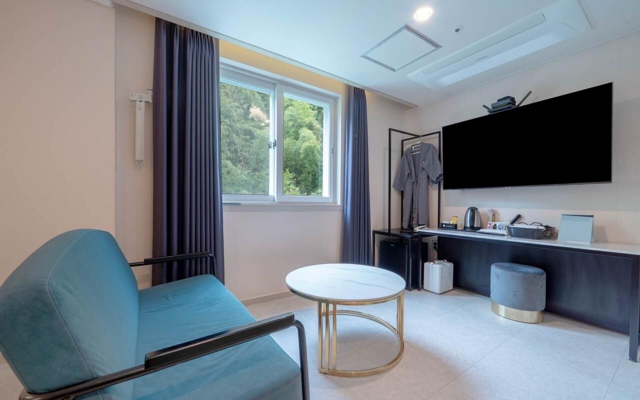 Une pièce moderne comprenant un canapé, une table ronde, un téléviseur, un bureau avec un ordinateur et une fenêtre avec des rideaux.