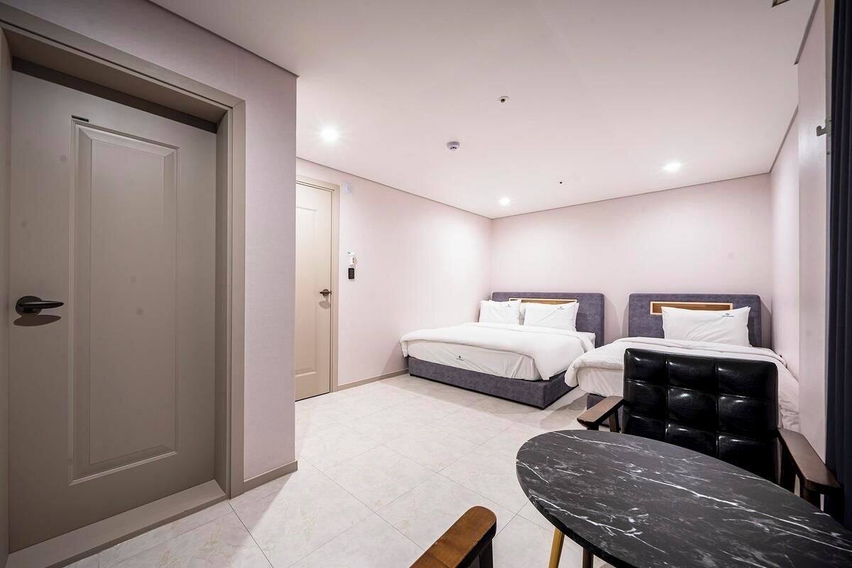 A bedroom with two beds, a table, and a bench.