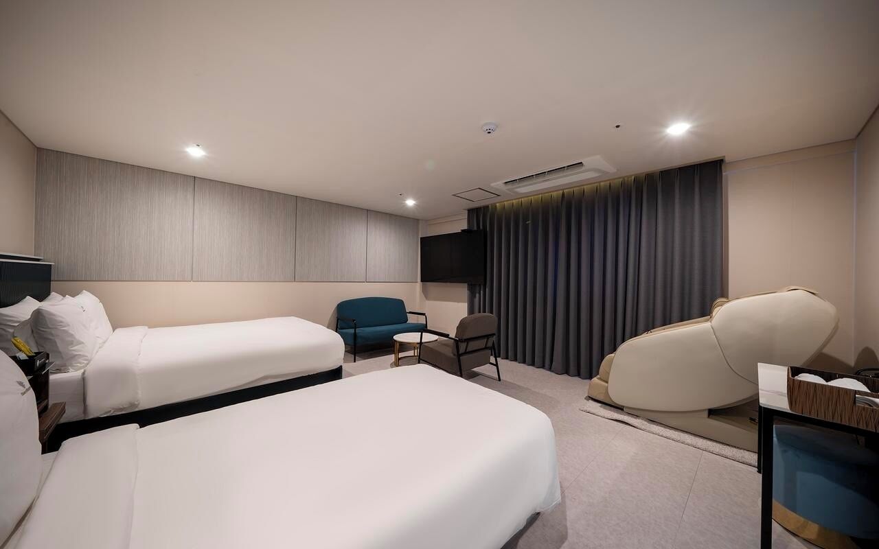 Una habitación de hotel con dos camas, un sofá, una silla, un televisor y una cortina.