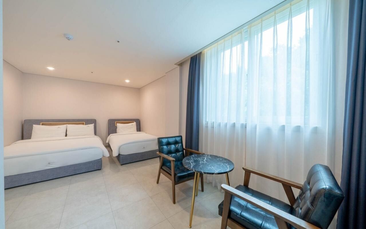 A hotel room with two beds, a round table, and a chair.