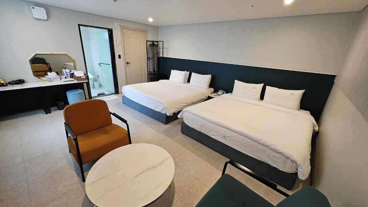 A hotel room with two beds, a desk, a chair, and a round table.