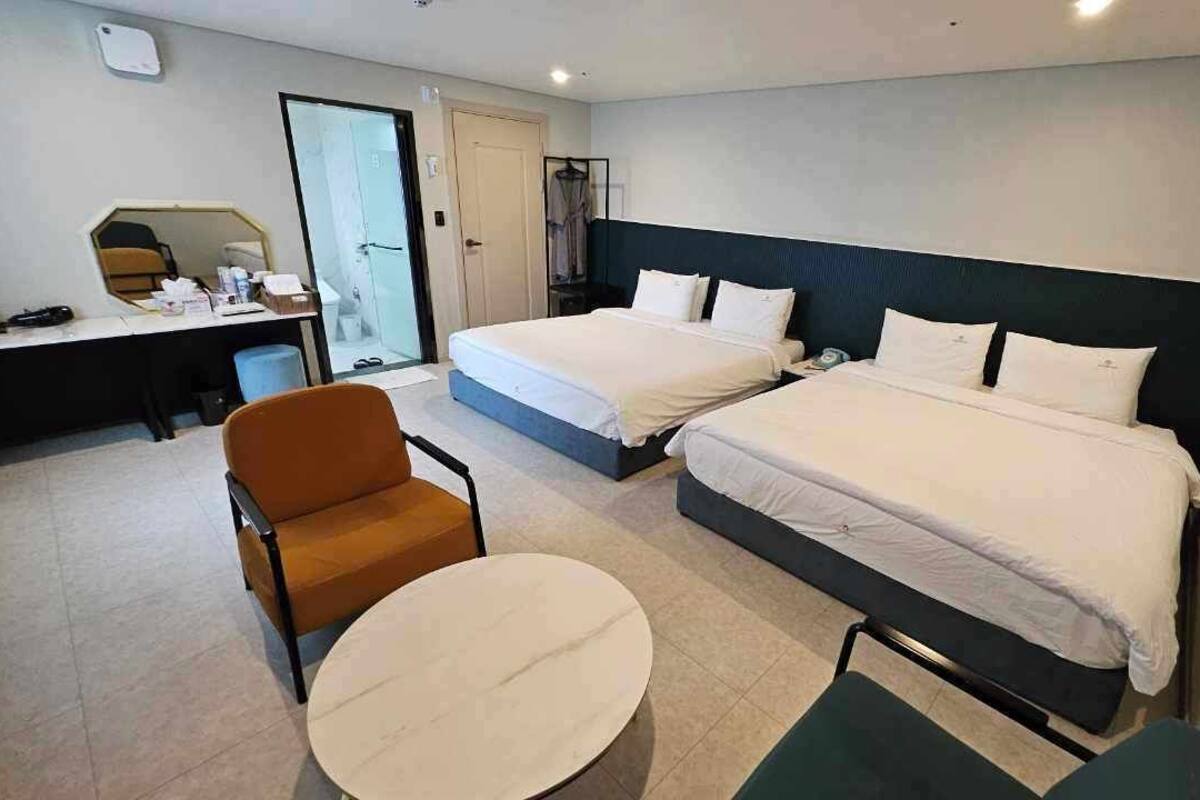 A hotel room with two beds, a desk, a chair, and a round table.
