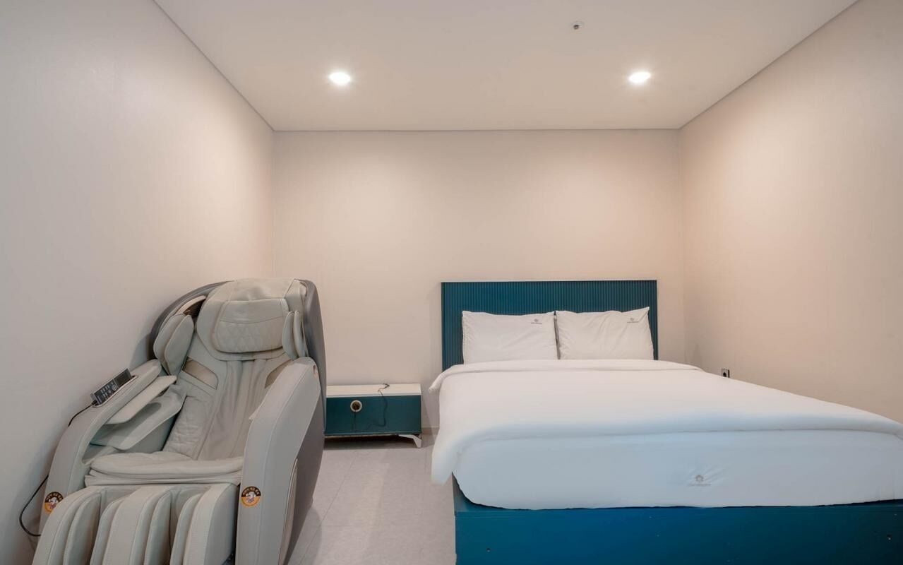 Un dormitorio con una silla de masaje, una cama con cabecera azul y una mesita de noche.
