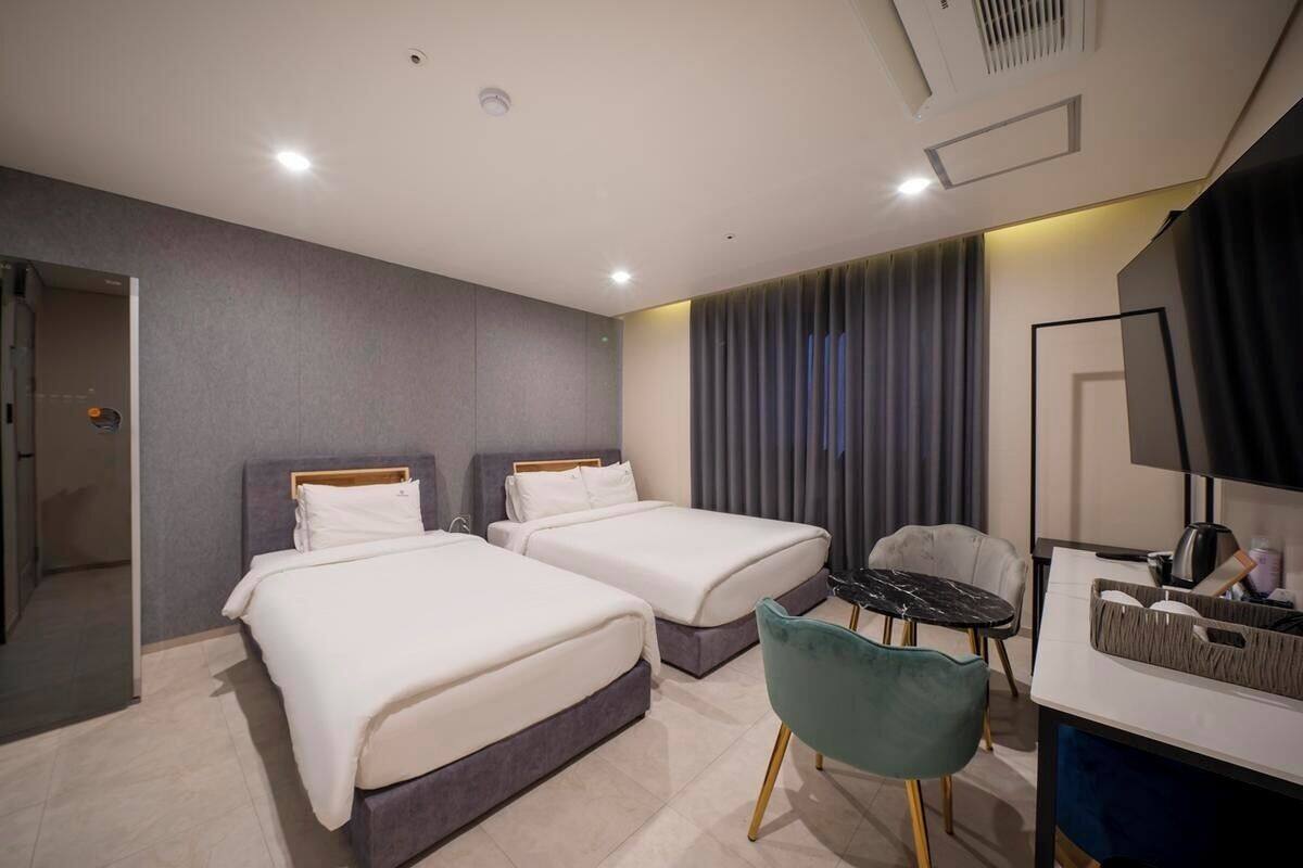 A hotel room with two beds, a desk, a chair, and a television.