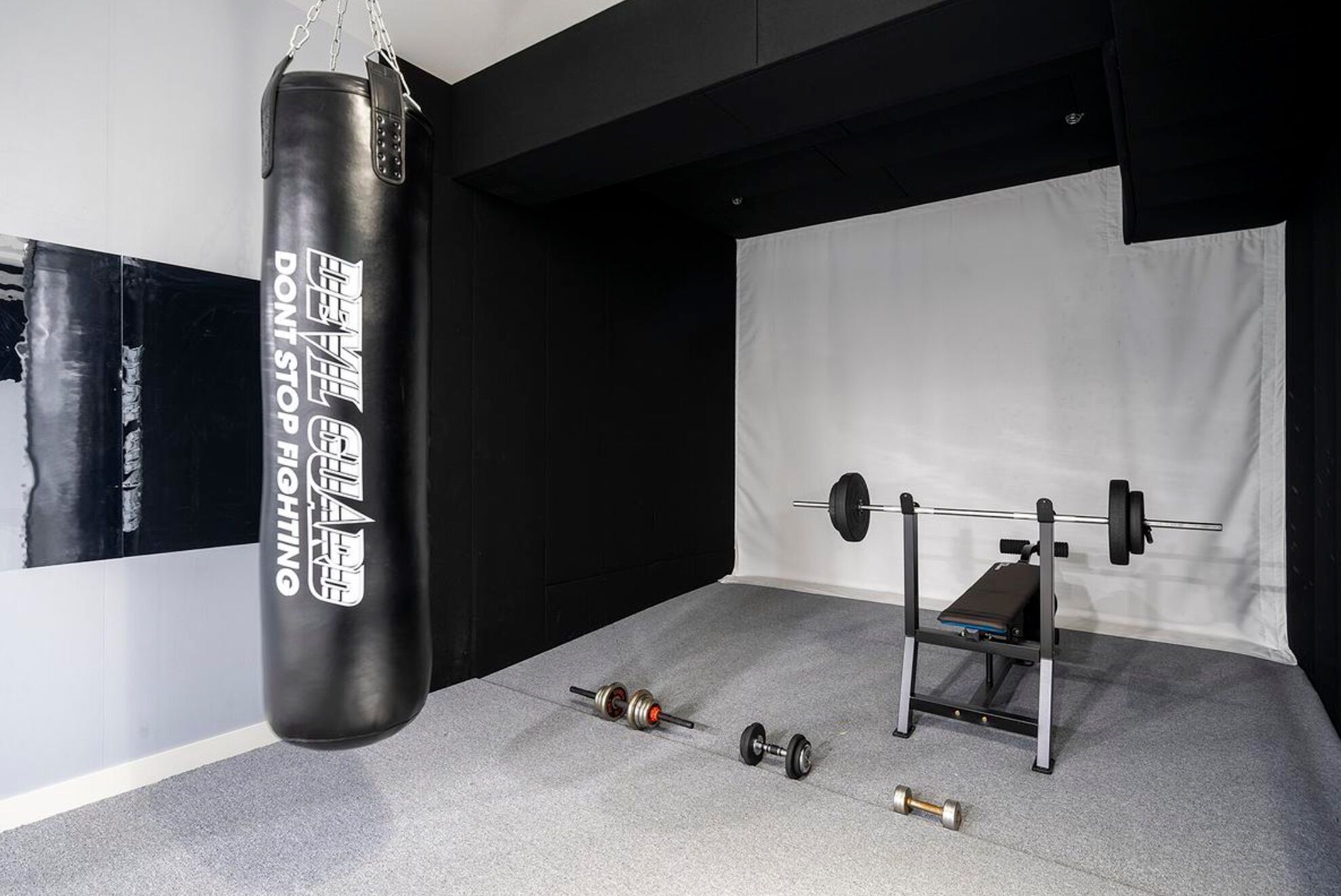 A gym with a punching bag, a barbell, and dumbbells.