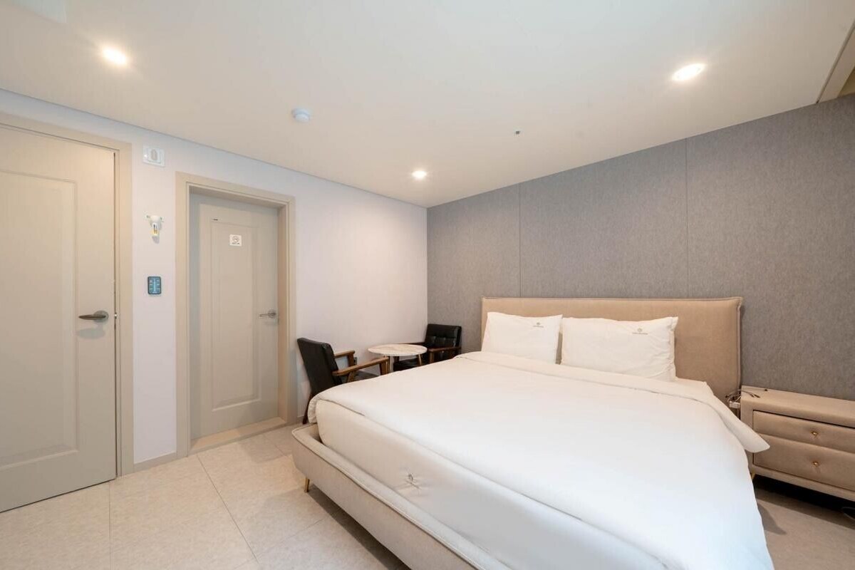 Ein modernes Hotelzimmer mit einem großen Bett, Nachttischen, einem kleinen Schreibtisch mit Stuhl und einer Tür.