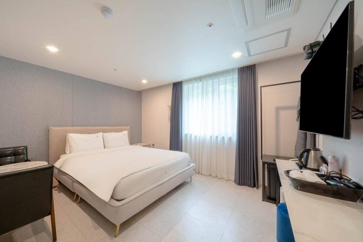 A hotel room with a bed, a desk, a chair, a TV, and a window with curtains.