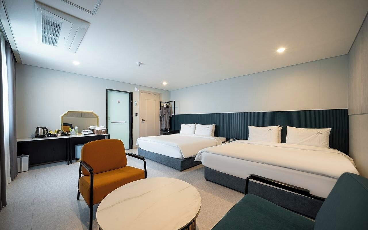 Una habitación de hotel con dos camas, un escritorio, una silla y una mesita.