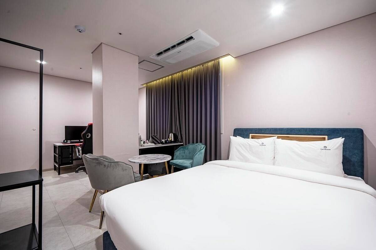A hotel room with a bed, a desk, a chair, a small table, and a curtain.