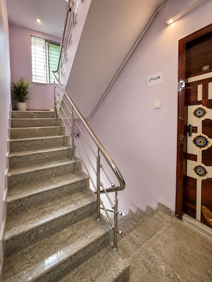 A staircase with metal railings, a potted plant, and a door with a decorative pattern. - Hotel Golden Regency (Kolkata)