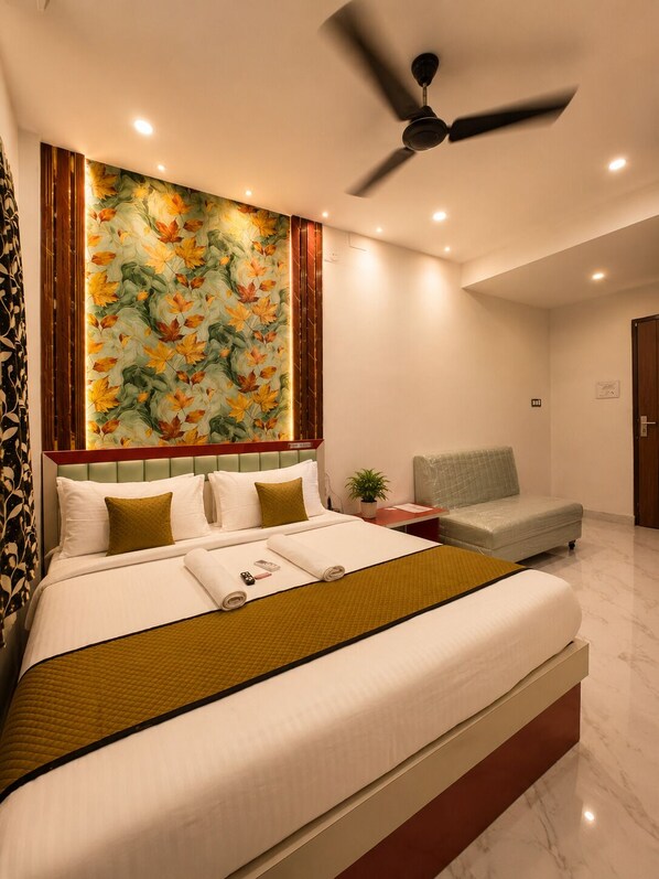 A hotel room with a bed, a ceiling fan, a wall with a floral mural, a small table, and a chair.
