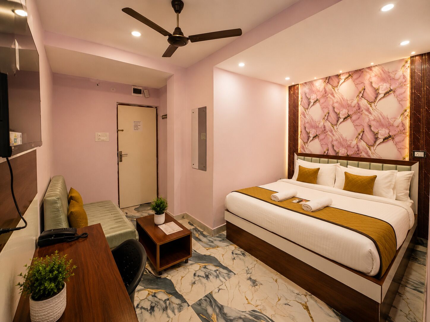 Habitación de hotel con cama, escritorio, silla, ventilador de techo y puerta.