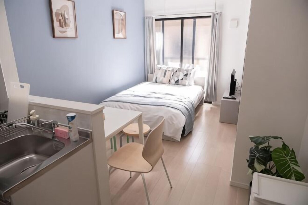 A compact hotel room with a bed, a small kitchenette, a dining area, and a large window.