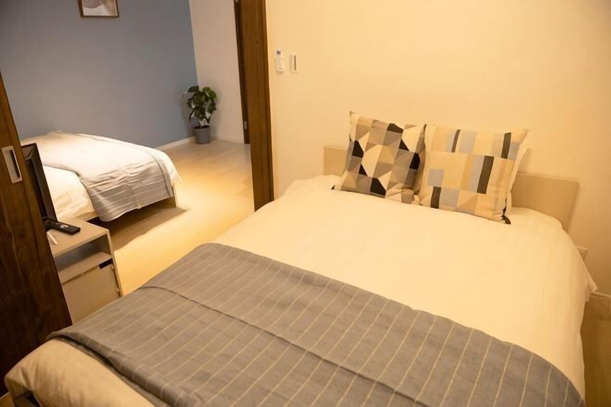 A bedroom with a bed, a bedside table, a chair, and a potted plant.