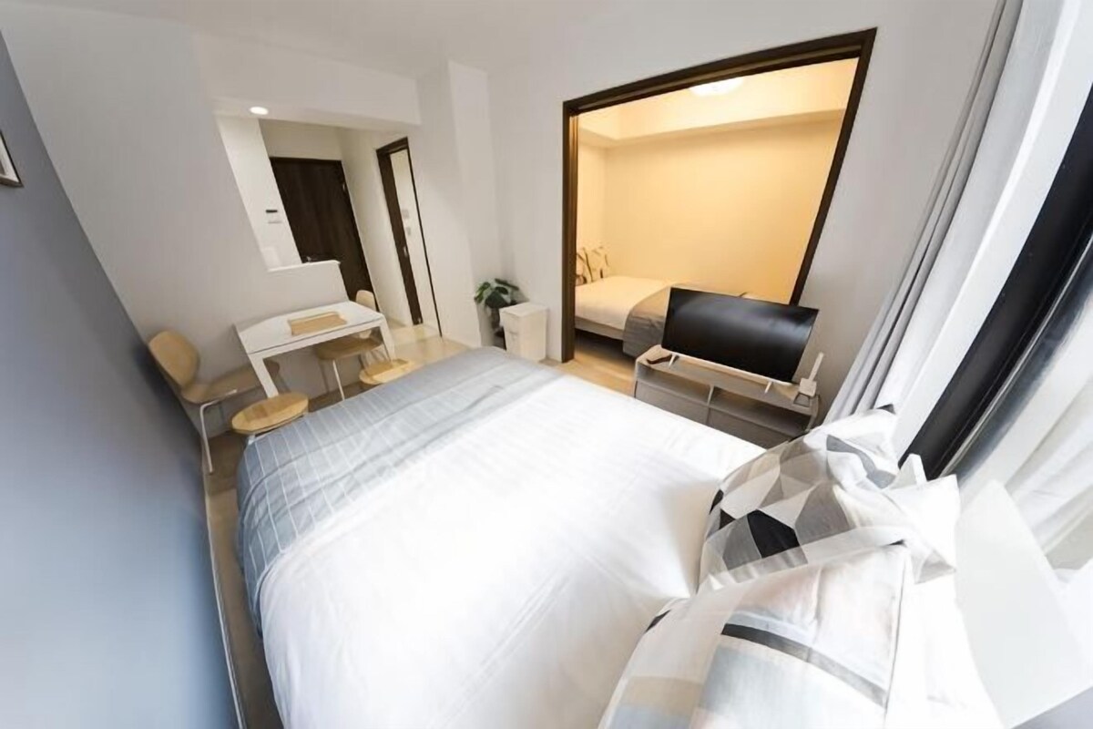 A modern hotel room with a bed, desk, chair, and a large window.