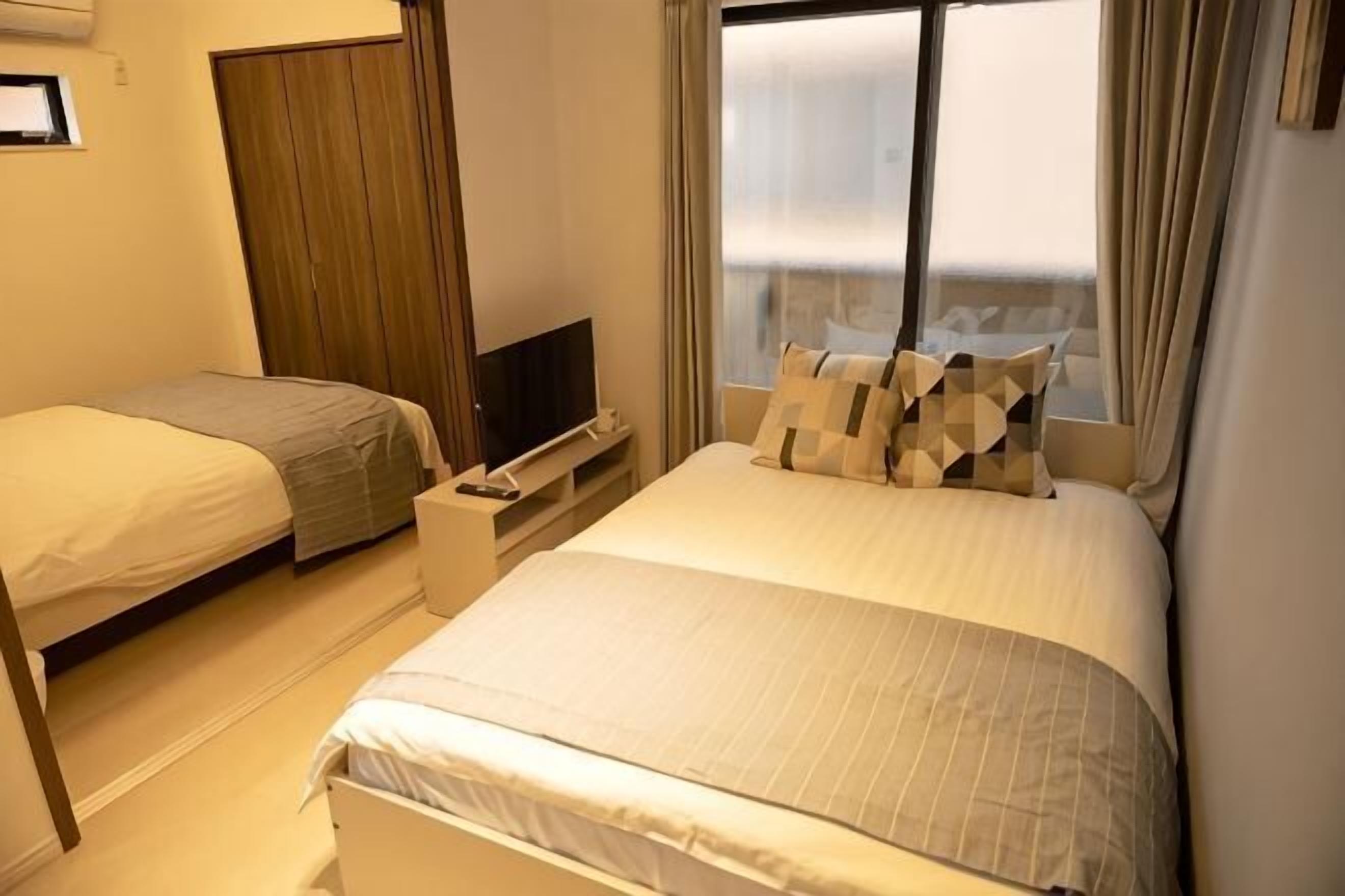 Ein Hotelzimmer mit zwei Einzelbetten, einem Fernsehgerät auf einem Standfuß und einem Fenster mit Vorhängen.