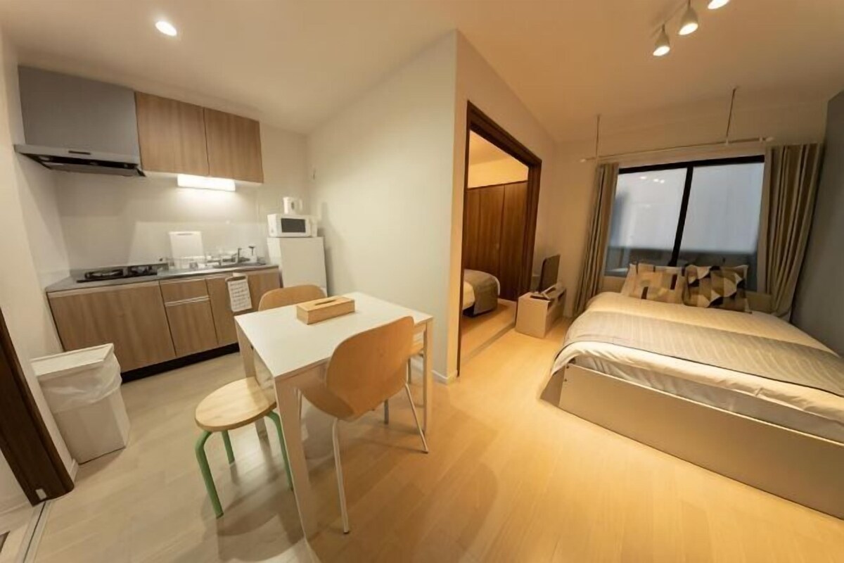 A compact hotel room with a kitchenette, a bed, a dining area, and a view of the city.