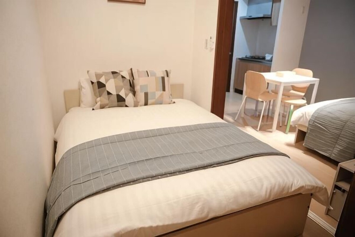 A bedroom with a bed, a bedside table, a chair, and a small table with a chair.