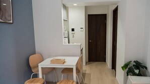 A small, modern room with a bed, a table with chairs, a mirror, and a door leading to another room. - Ashe Maison Tennoji West II (Osaka)