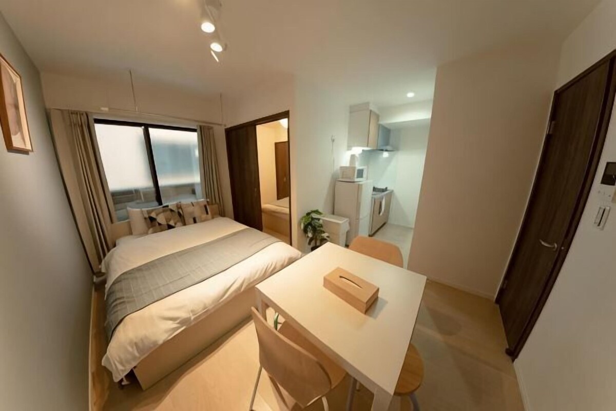 A bedroom with a bed, a desk, and a kitchenette.