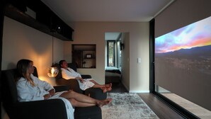 Una camera moderna con una grande TV che mostra una vista al tramonto, un divano, un tavolino e una mensola a parete.