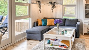 A modern living room with a sectional sofa, a glass coffee table, and a view through large windows.