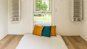 A bedroom with a bed, two pillows, a window, and a view of a car and greenery outside.