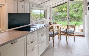 A kitchen with white cabinetry, a black stove, and a dining area with wooden furniture. - 3 bedroom amazing home in Brovst (Brovst)