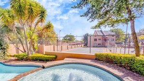A swimming pool with a hot tub, surrounded by palm trees and a fence. - Sandton 2 bed apartment (Sandton)