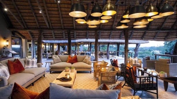 An outdoor lounge area with sofas, chairs, and tables, featuring a thatched roof and hanging pendant lights. - Sandton 2 bed apartment (Sandton)