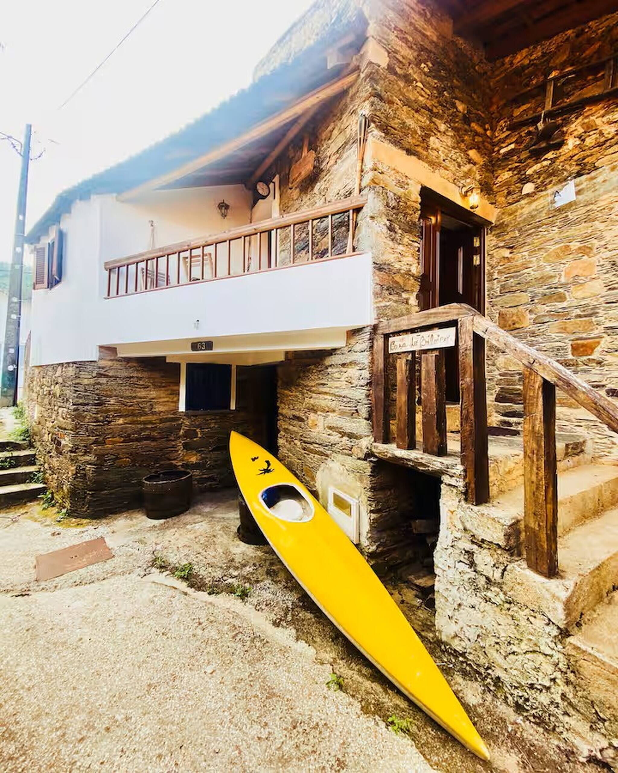 A stone building with a white upper level and a yellow kayak leaning against it.