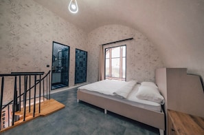 Um quarto com cama, escada de madeira, janela e porta.