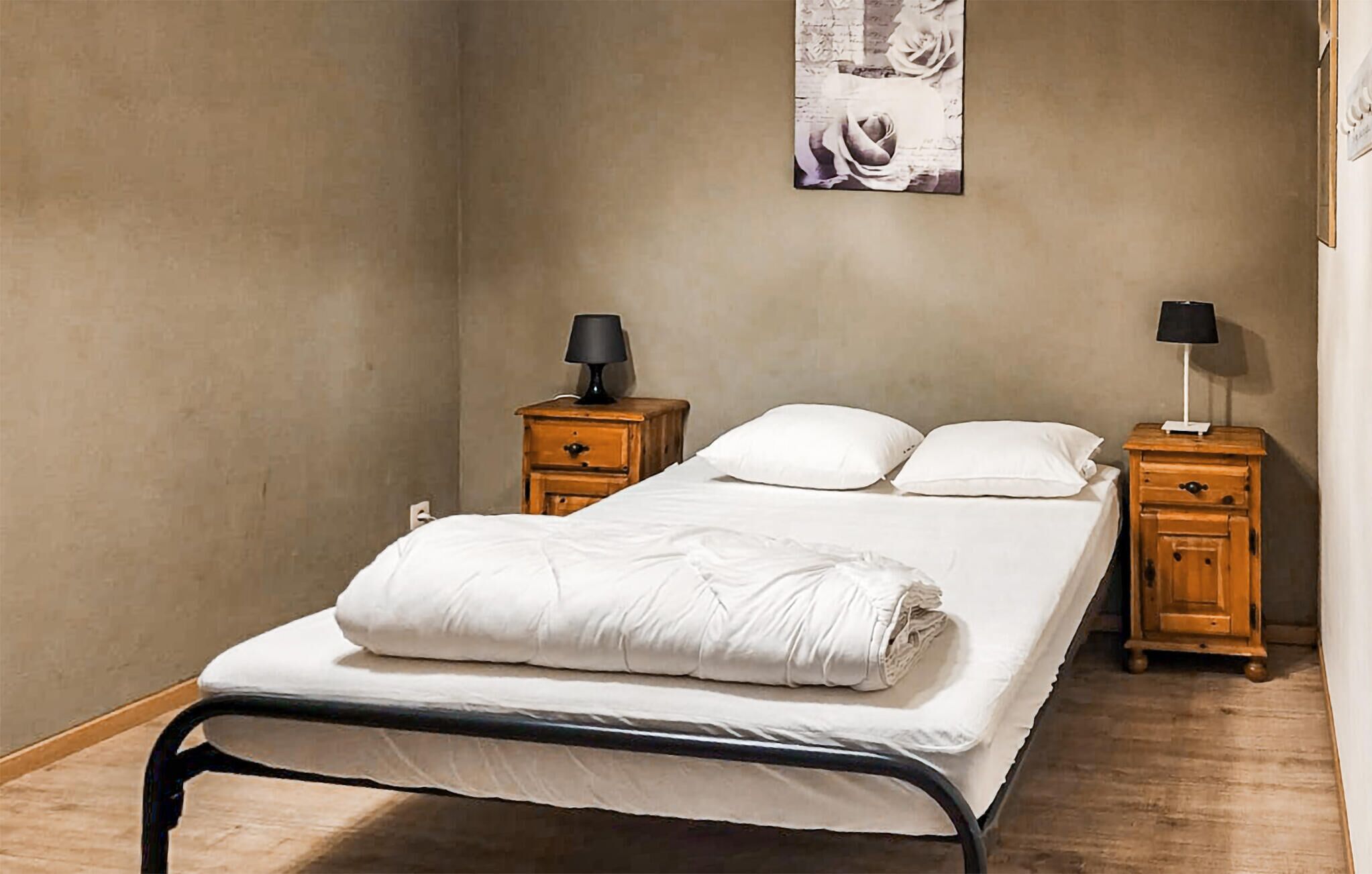 A single bed with a metal frame, two bedside tables with lamps, and a wall-mounted picture.