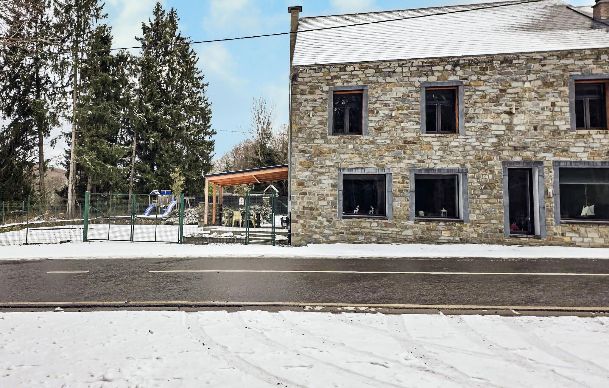 Un bâtiment en pierre doté de nombreuses fenêtres, une aire de jeux clôturée avec des toboggans et un sol recouvert de neige.