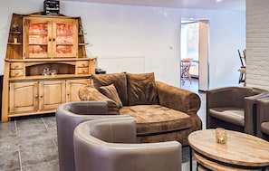 Ein Wohnzimmer mit einem braunen Ledersofa, zwei Sesseln, einer Holzkommode mit Gläsern und einem runden Holztisch.