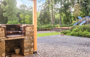 Ein Steingrill, eine gepflasterte Terrasse und ein Spielplatz mit einer Rutsche.