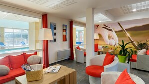 En hotellobby med utsikt över poolen, möbler i rotting och röda detaljer.