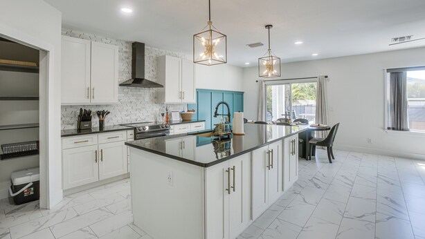 A modern kitchen with white cabinetry, a central island, and pendant lighting. - Ever After | Once Upon A Vacation (Cape Coral)