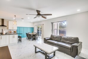 Eine moderne Küche mit weißen Schränken, ein Essbereich mit Tisch und Stühlen, ein Ledersofa und ein Deckenventilator.