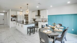 A modern kitchen with white cabinetry, a central island, and a dining area with a round table and chairs. - Ever After | Once Upon A Vacation (Cape Coral)